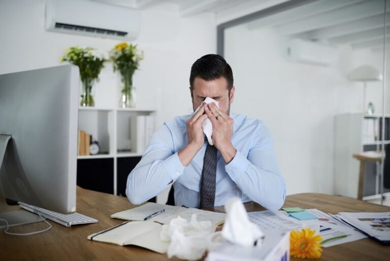 sick businessman blowing nose at desk