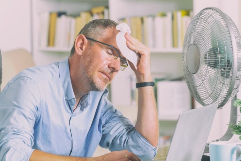 Man wiping sweat from his face in front of a fan